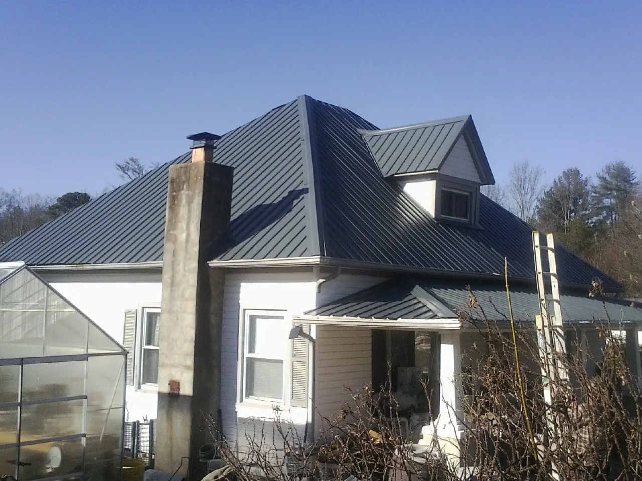 Dark blue standing seam metal roof on a white farmhouse with dormer — Slate & Tile Roof Repair by Roofing Brothers in Grand Coteau