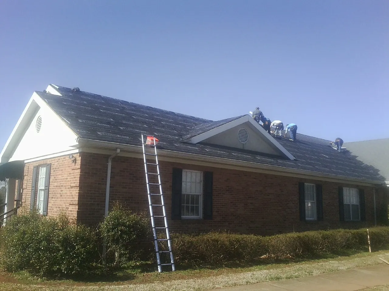 Crew tearing shingles off a brick ranch roof with a ladder set — Metal Roof Repair work by our crew in Grand Coteau