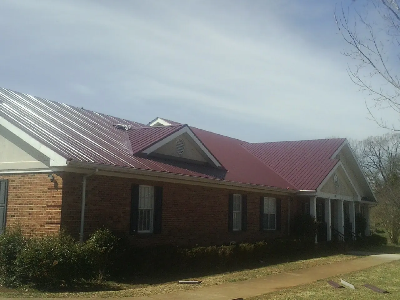 Red metal roof with gabled entries on a long brick building, from a Hail Damage Roof Repair job in Grand Coteau