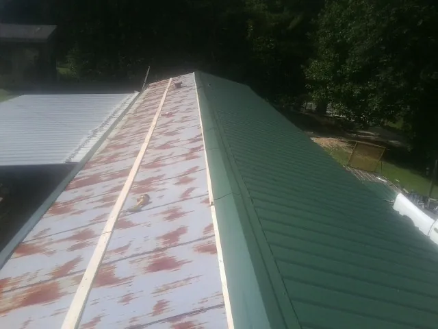 Old rusted panels beside newly installed green metal roofing — Wind Damage Roof Repair by Roofing Brothers in Grand Coteau