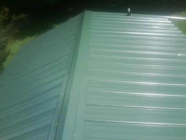 New green metal panels meeting at the ridge of a roof — Flat Roof Repair work by our crew in Grand Coteau