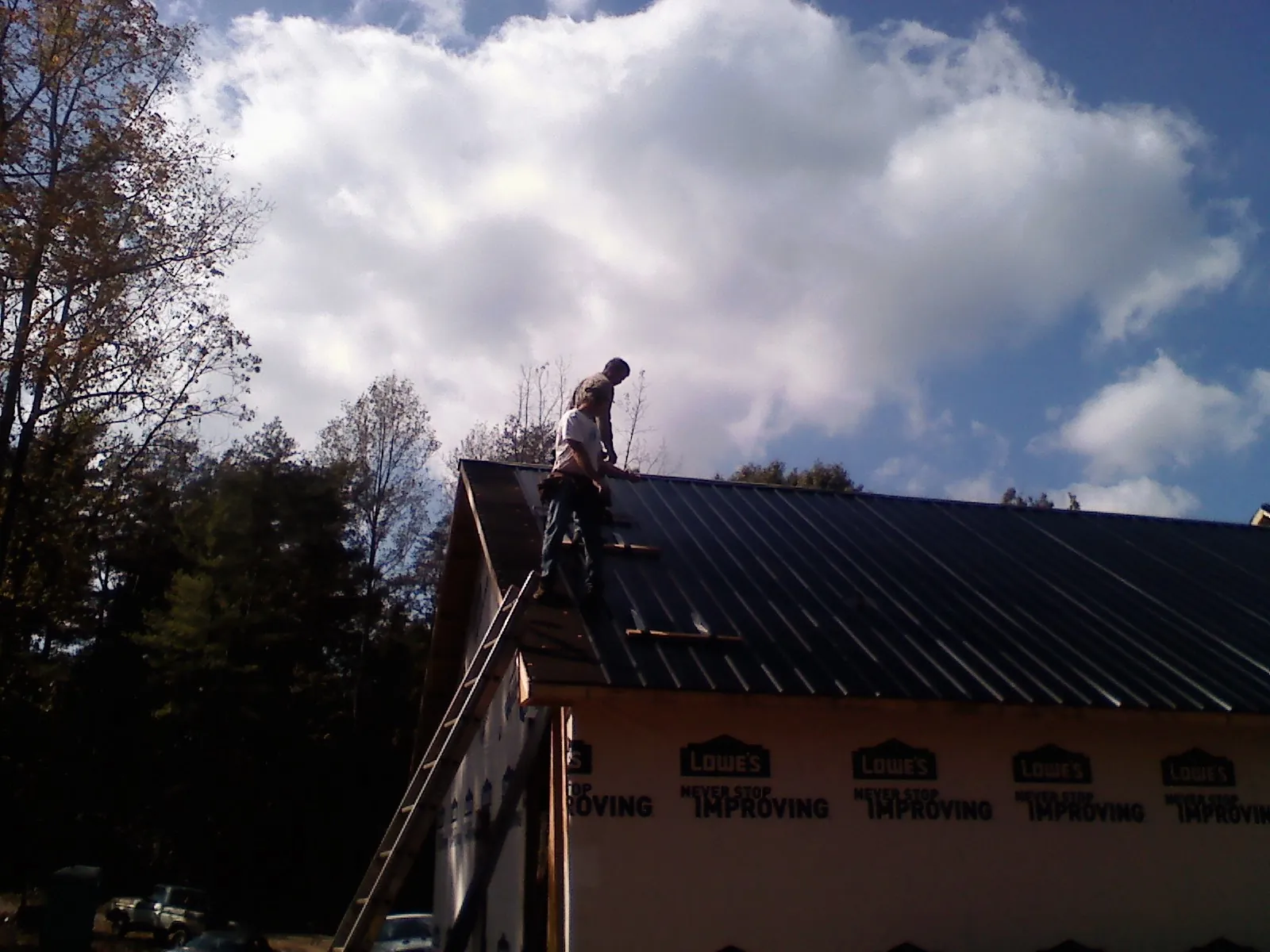 Roofer fastening dark metal panels high against a cloudy sky, from a Roof Inspection job in Grand Coteau