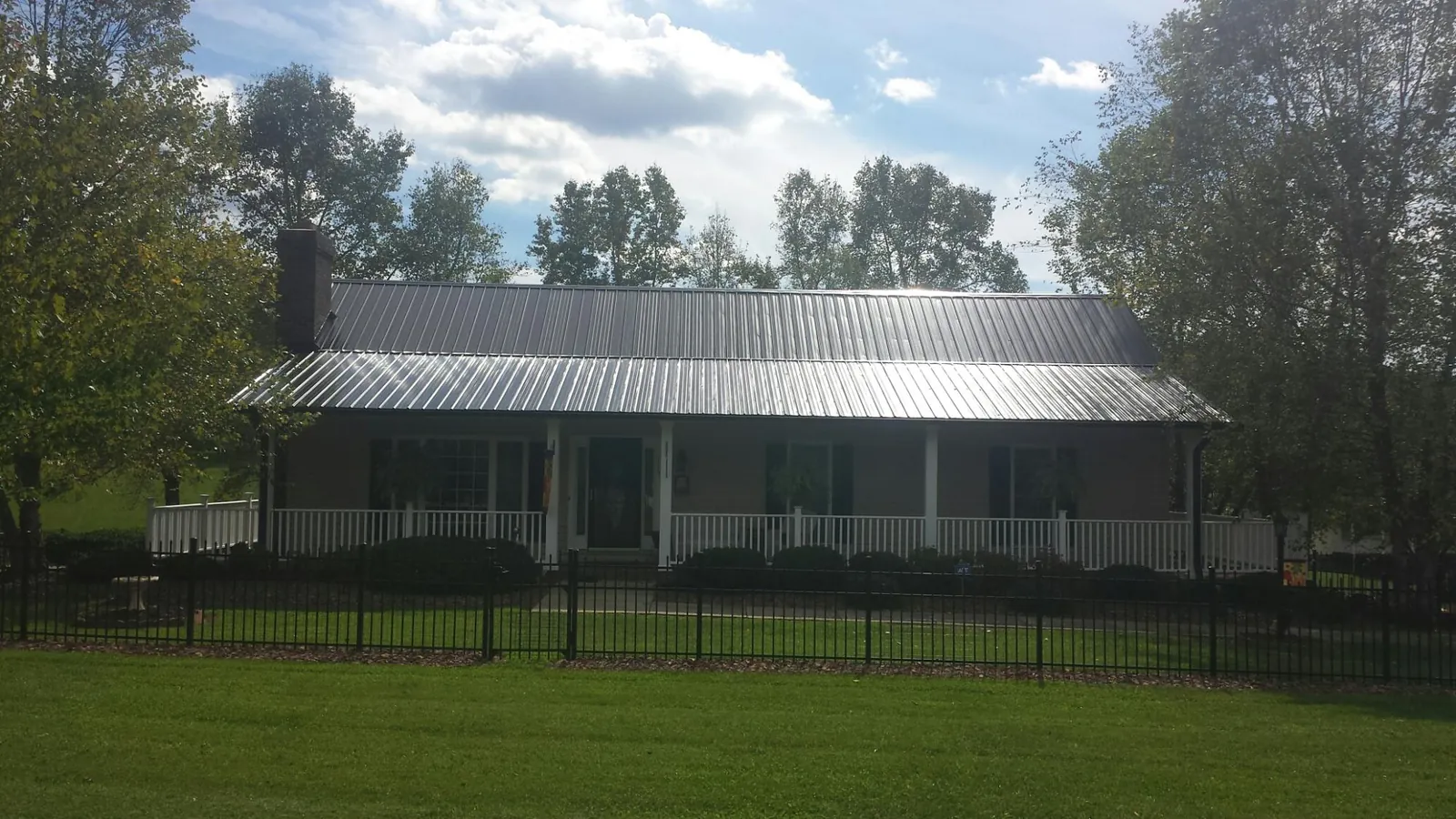 Gray metal roof on a brick ranch with a full width front porch — Gutter Guard Installation work by our crew in Grand Coteau