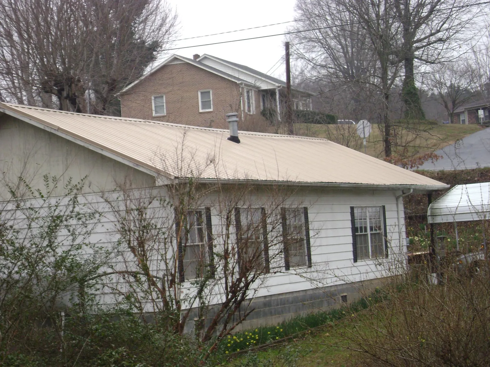 Tan metal roof on a white sided house set into a hillside — Commercial Roofing by Roofing Brothers in Grand Coteau