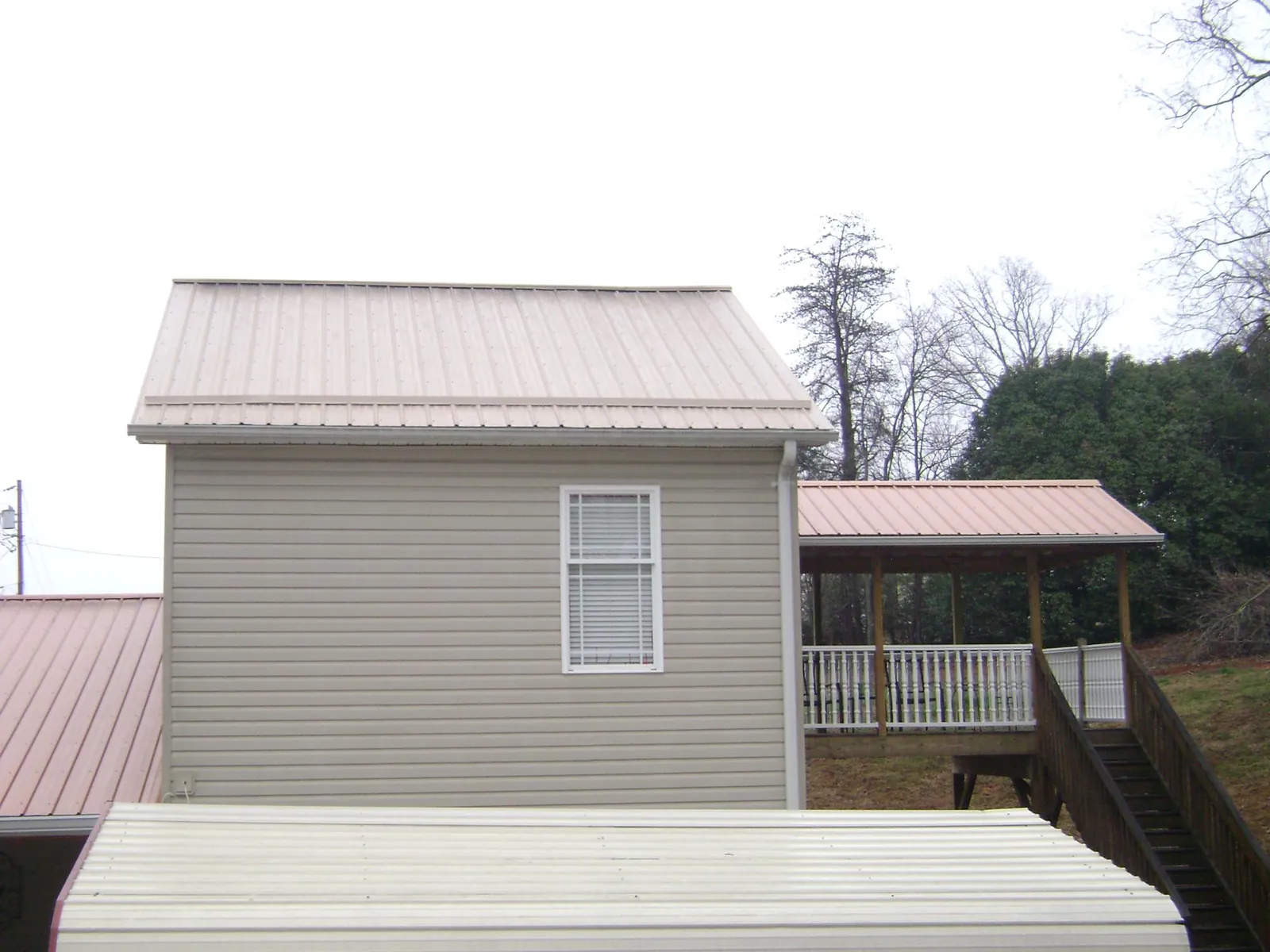 Tan metal roofs on a two story addition and attached porch, from a Roof Replacement job in Grand Coteau